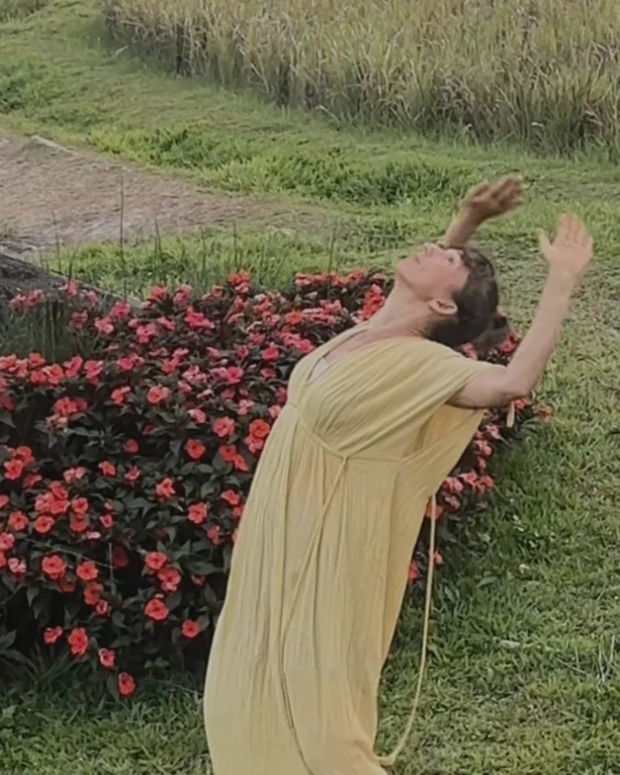 Lola expanding through an open chest movement in a yellow dress outdoors